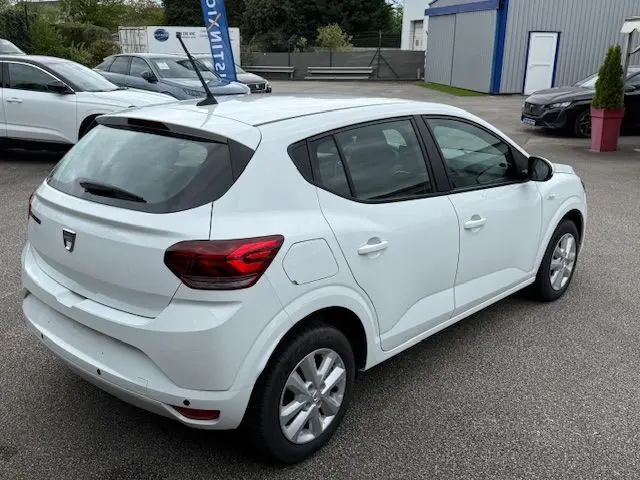 Vue 3/4 arrière droite d'une Dacia Sandero blanche Glacier 2023, compacte avec feux arrière rouges et antenne sur le toit.