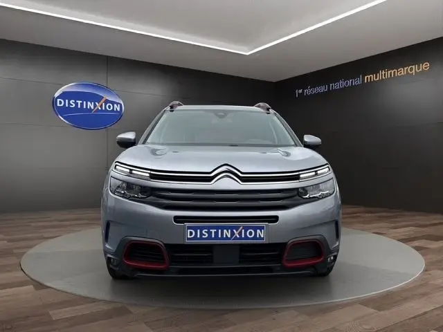 Vue frontale d'un Citroën C5 Aircross gris clair avec détails rouges sur le pare-chocs, en showroom Distinxion.