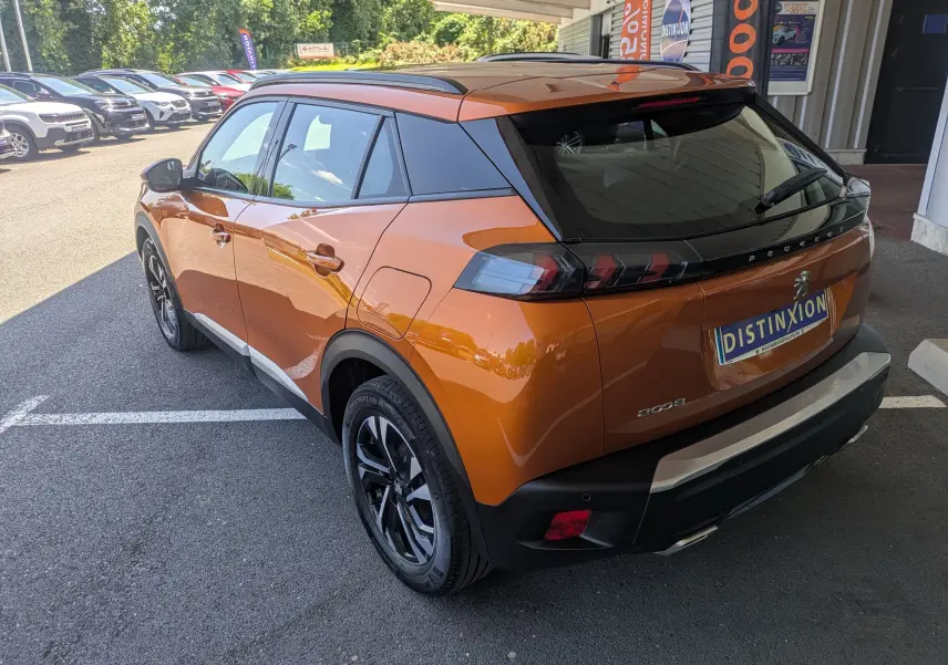 Vue 3/4 arrière droite d'un Peugeot 2008 orange 2021 avec jantes noires bicolores et toit noir, stationné en extérieur.