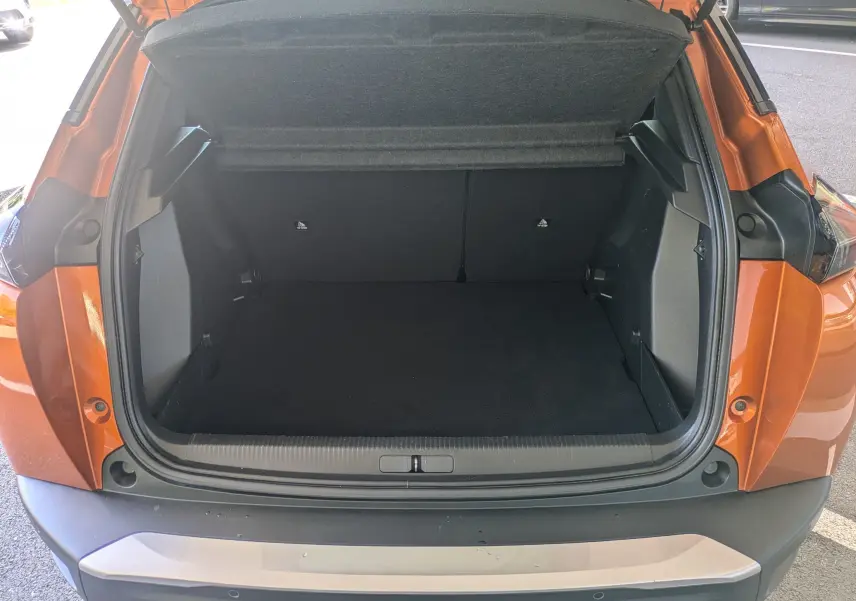Coffre ouvert vu de l'arrière d'un Peugeot 2008 orange, montrant un espace de chargement vide et propre.