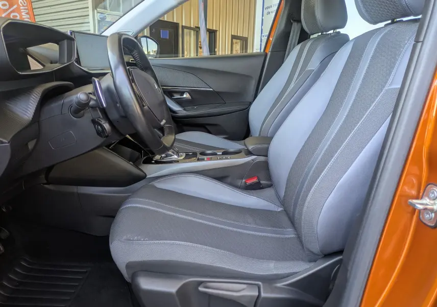 Vue intérieure côté conducteur de la Peugeot 2008 orange 2021, montrant les sièges gris et la console centrale avec boîte automatique.