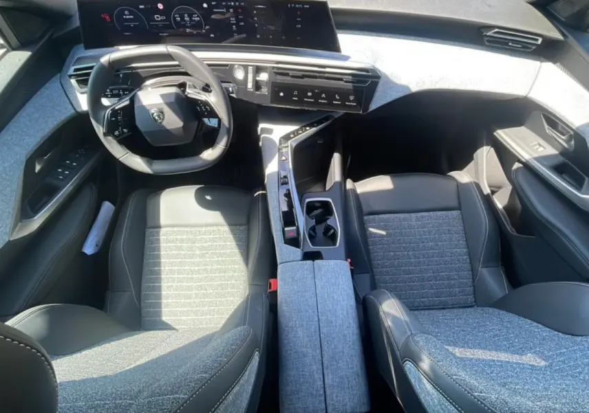 Vue intérieure de face du Peugeot 3008 2025, sièges tissu gris et cuir noir, tableau de bord numérique et console centrale moderne.