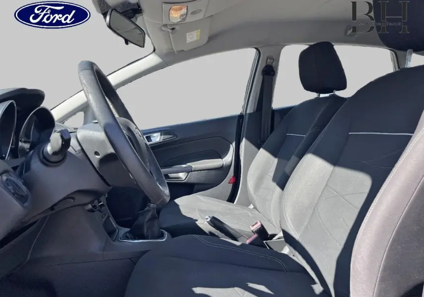 Vue intérieure côté conducteur de la Ford Fiesta 1.5 TDCi 75ch Edition 2015 avec sièges tissu noirs et volant cuir multifonction.