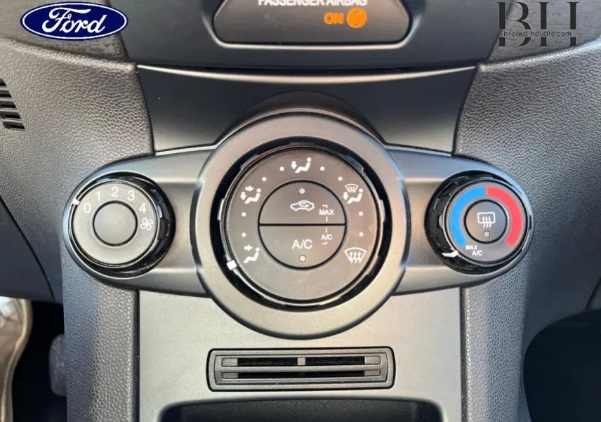 Gros plan sur les commandes de climatisation manuelle d’une Ford Fiesta noire, avec réglages ventilation et température visibles.