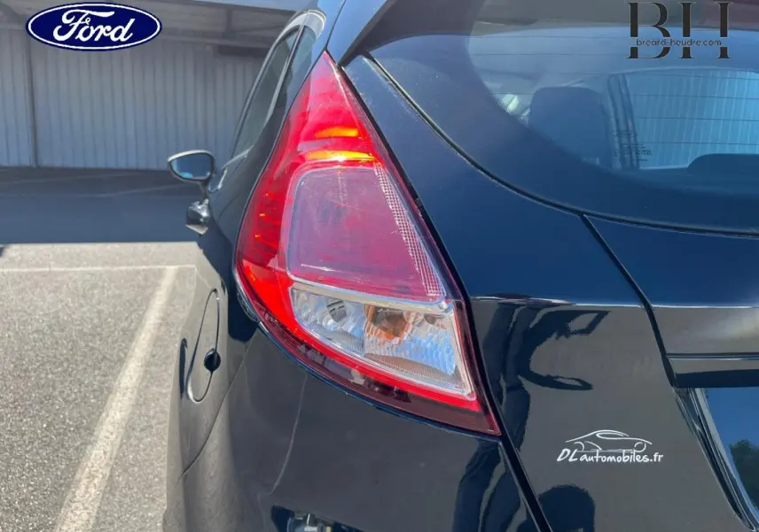 Vue 3/4 arrière gauche d'une Ford Fiesta noire Scala avec feu arrière distinctif et logo DLautomobiles.fr sur le coffre.