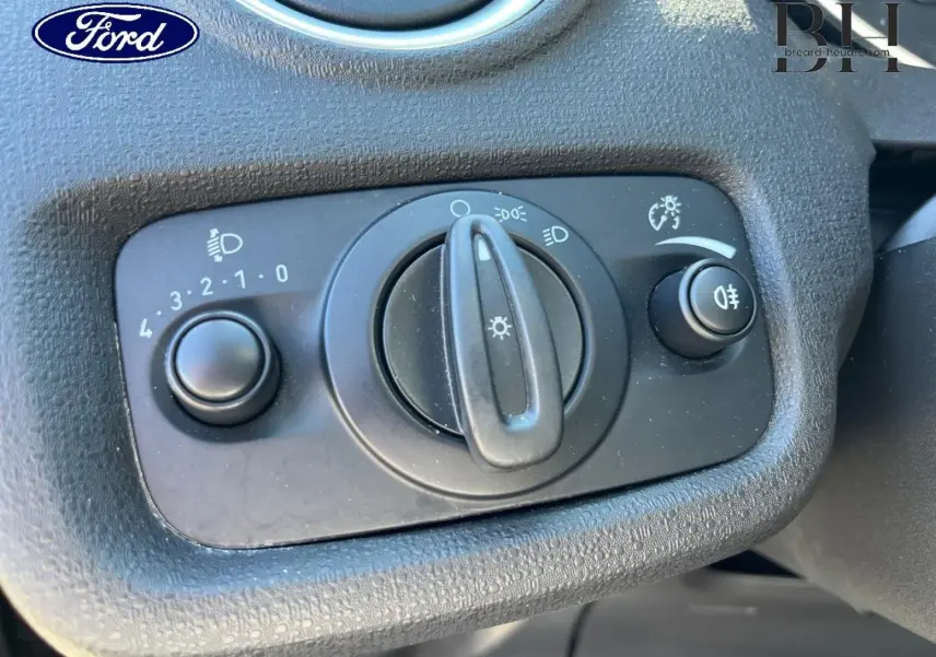 Gros plan sur le bouton de commande des phares du tableau de bord d'une Ford Fiesta noire, avec réglage d'intensité et feux antibrouillard.