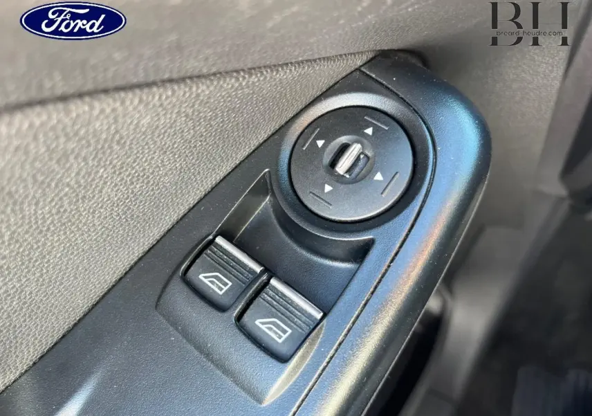 Gros plan sur les commandes électriques des vitres et réglage des rétroviseurs côté conducteur d'une Ford Fiesta noir Scala.