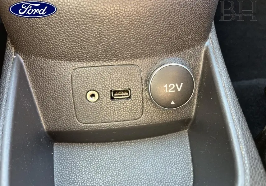 Vue rapprochée de la prise 12V, port USB et entrée auxiliaire sur la console centrale d'une Ford Fiesta noire.