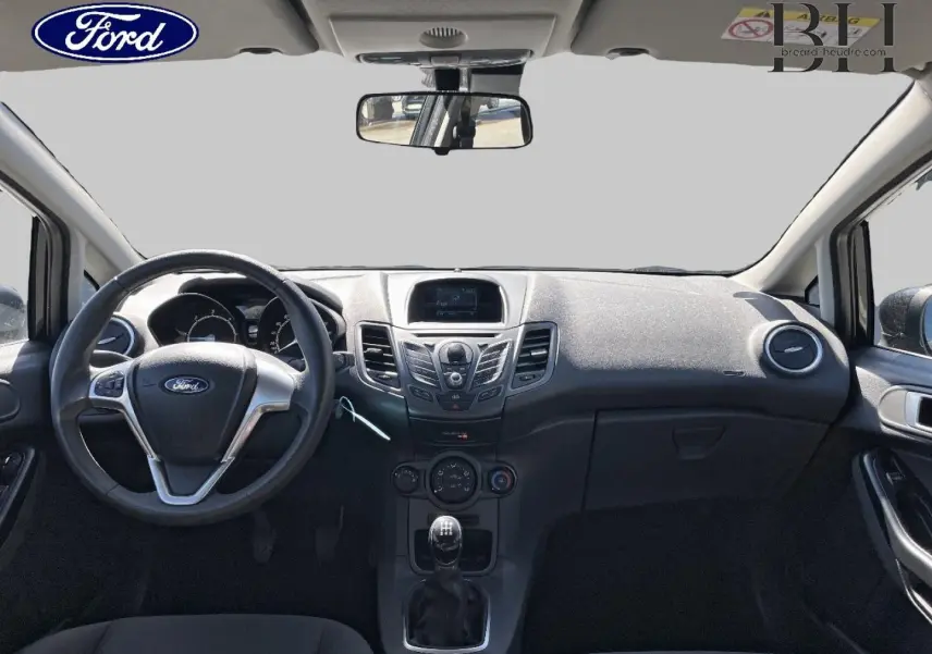 Vue frontale de l'intérieur noir de la Ford Fiesta 2015, montrant le volant multifonction et la console centrale avec écran.