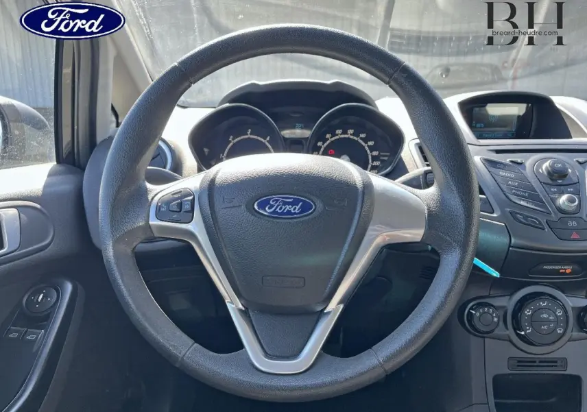 Vue centrée sur le volant multifonction noir de la Ford Fiesta 2015, avec tableau de bord et console centrale visibles.