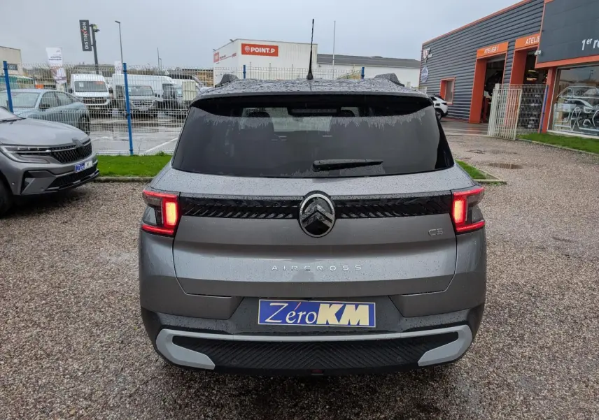 Vue arrière du Citroën C3 Aircross gris métallisé avec toit noir et feux arrière LED allumés sur parking humide.