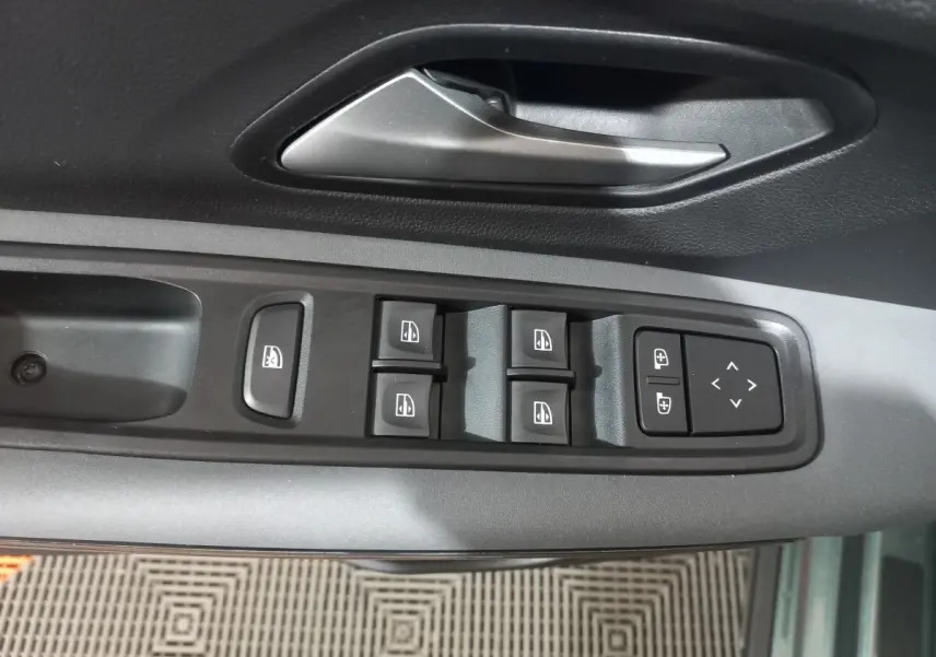 Vue rapprochée des commandes de lève-vitres et rétroviseurs sur la portière côté conducteur d'une Dacia Sandero 2024 vert.