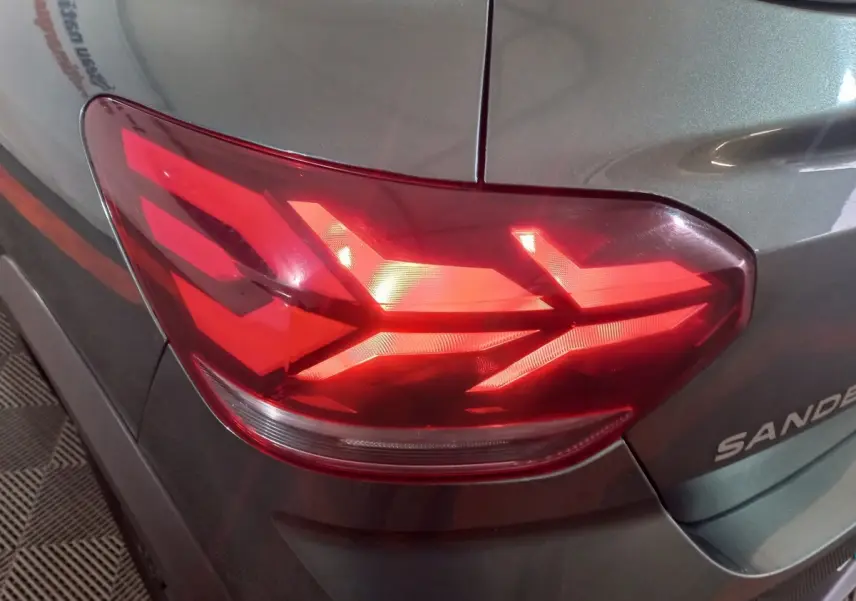 Gros plan sur le feu arrière droit rouge d'une Dacia Sandero 2024 vert foncé, avec logo partiel visible sur la malle.
