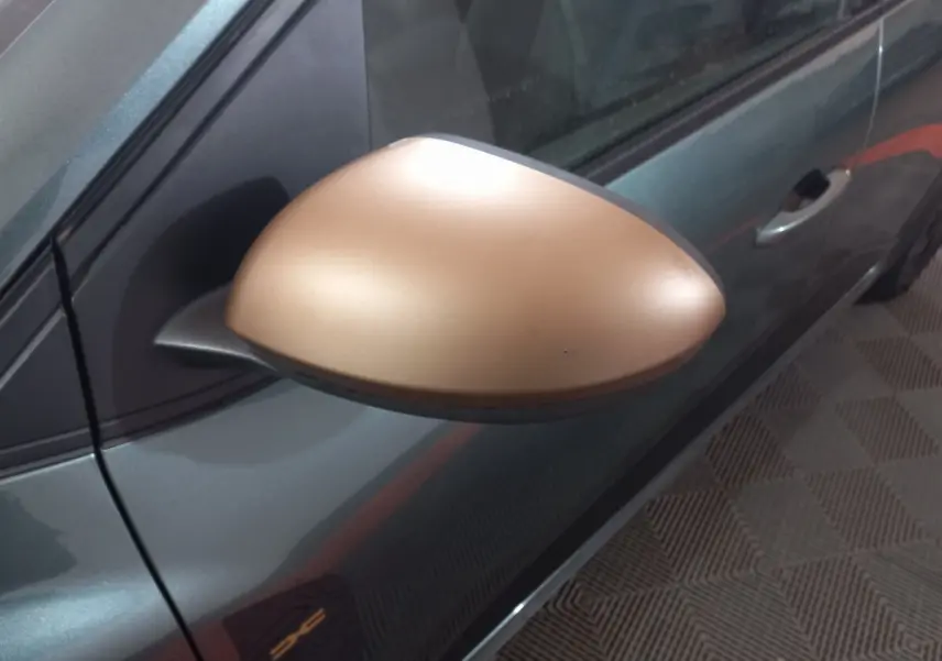 Gros plan sur le rétroviseur droit doré d'une Dacia Sandero 2024 vert foncé, avec poignée de porte visible.