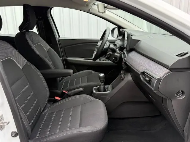 Intérieur avant de la Dacia Sandero blanc glacier 2023, vue côté conducteur, sièges noirs et tableau de bord moderne.