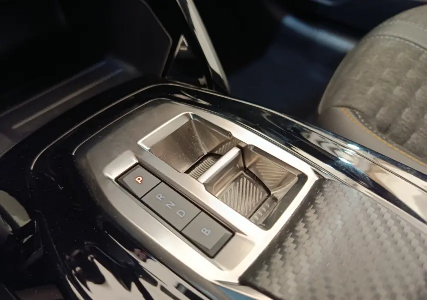 Gros plan sur la console centrale noire brillante avec levier de vitesses automatique de la Peugeot 208 électrique gris clair.