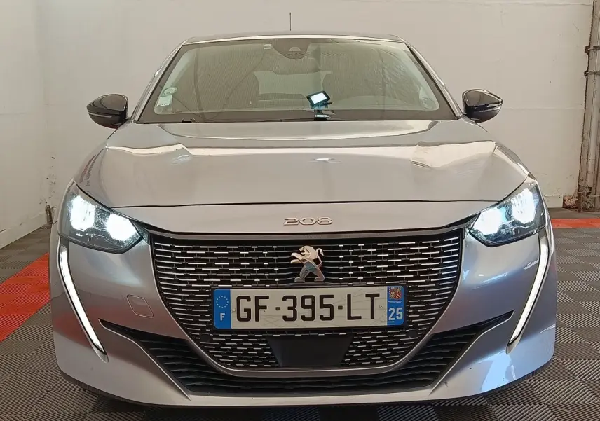 Vue de face du Peugeot 208 Electrique Roadtrip gris clair avec phares LED allumés et calandre distinctive.