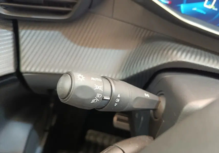 Gros plan sur la commande des phares et clignotants dans l'habitacle du Peugeot 208 électrique gris clair, version 2022.