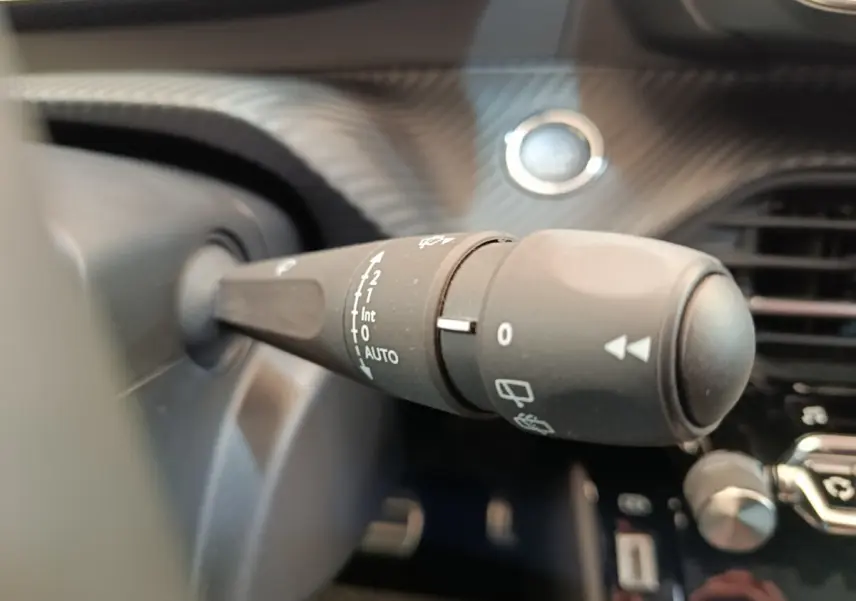 Gros plan sur la commande d’essuie-glace à gauche du volant dans l’habitacle d’une Peugeot 208 électrique gris clair.