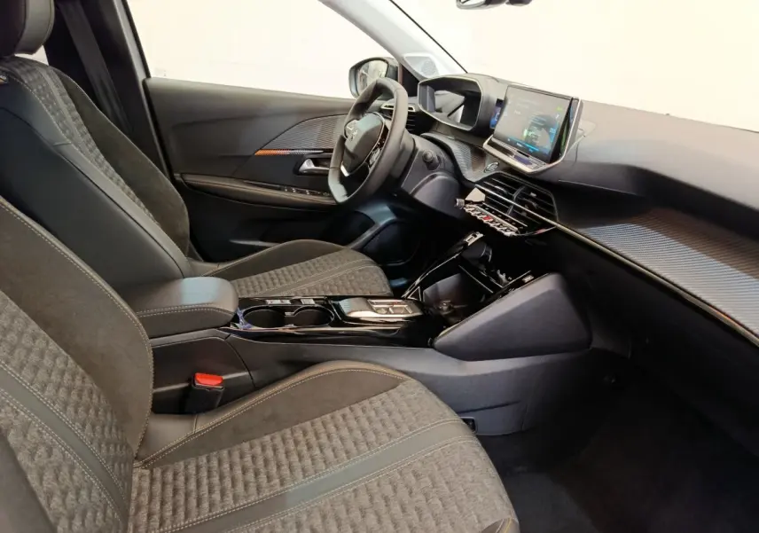 Intérieur avant droit de la Peugeot 208 électrique, sièges gris, tableau de bord avec écran tactile et volant cuir.
