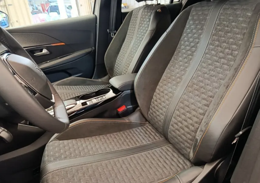 Vue intérieure côté conducteur des sièges avant gris foncé avec surpiqûres orange et volant cuir de la Peugeot 208 Electrique Roadtrip 2022.