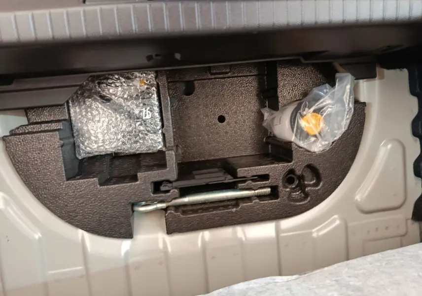 Compartiment de rangement sous le plancher de coffre de la Peugeot 208 électrique gris clair, avec outils et accessoires emballés.