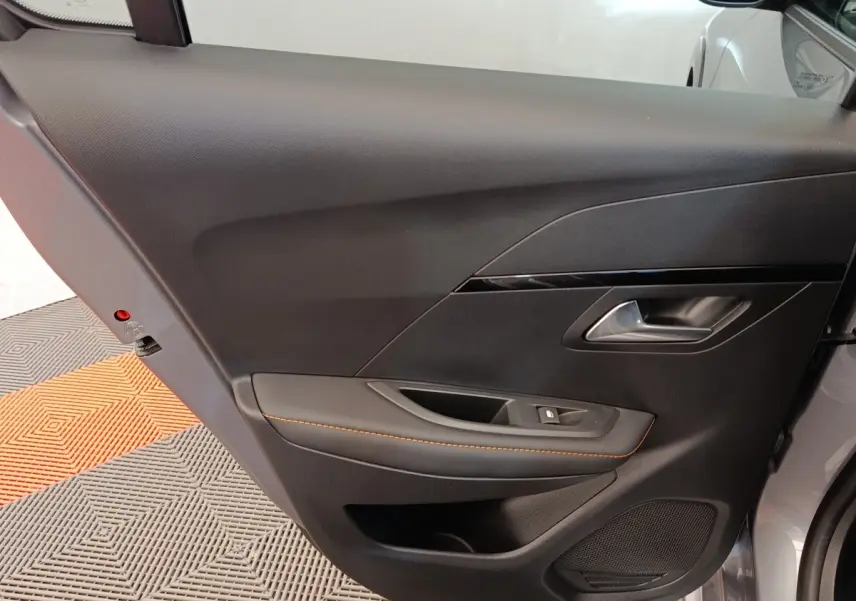 Intérieur côté gauche de la porte avant d’une Peugeot 208 électrique gris clair avec surpiqûres orange.