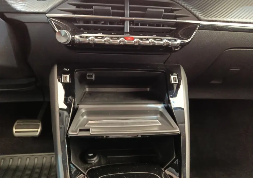 Vue rapprochée du tableau de bord central noir brillant de la Peugeot 208 Electrique ROADTRIP 2022, avec commandes et prises USB visibles.