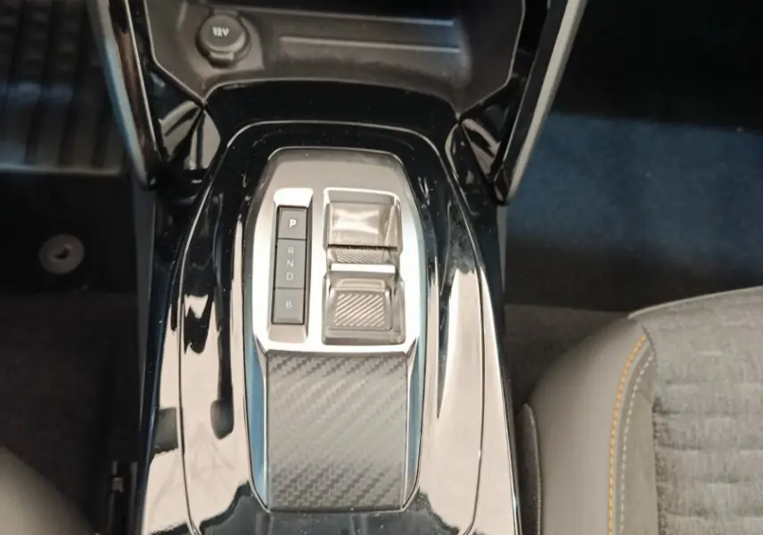Vue plongeante sur la console centrale noire brillante de la Peugeot 208 électrique avec levier de vitesse automatique et frein à main électrique.