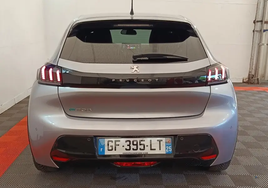 Vue arrière d'une Peugeot 208 électrique gris clair avec feux LED caractéristiques allumés en intérieur.