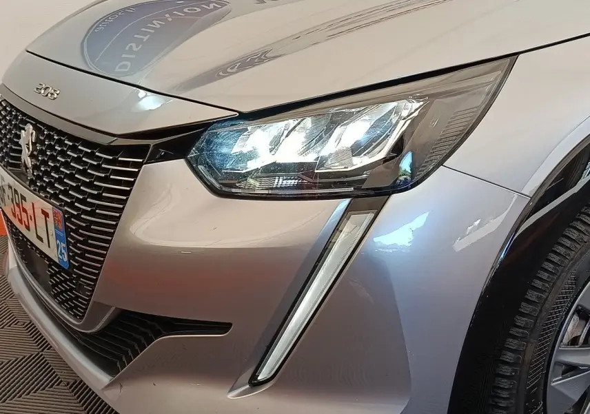 Gros plan sur l'avant droit gris clair de la Peugeot 208 Electrique ROADTRIP 2022 avec phares LED allumés et calandre noire.