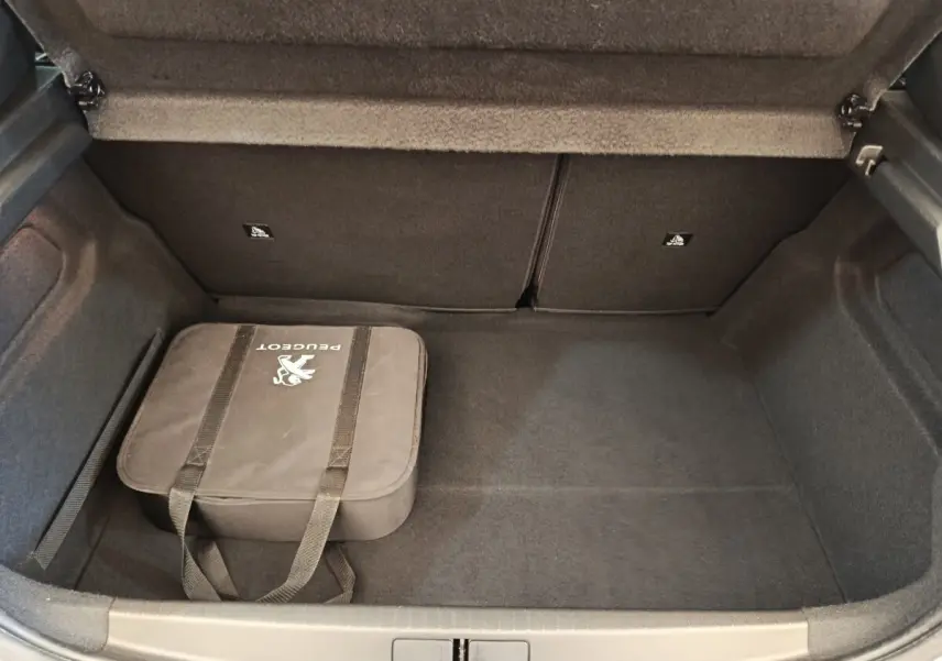Coffre ouvert de la Peugeot 208 Electrique gris clair, montrant un sac Peugeot noir à l'intérieur.