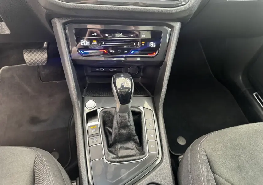 Vue intérieure centrée sur la console centrale du Volkswagen Tiguan gris clair, avec levier de vitesse automatique et commandes climatisation.