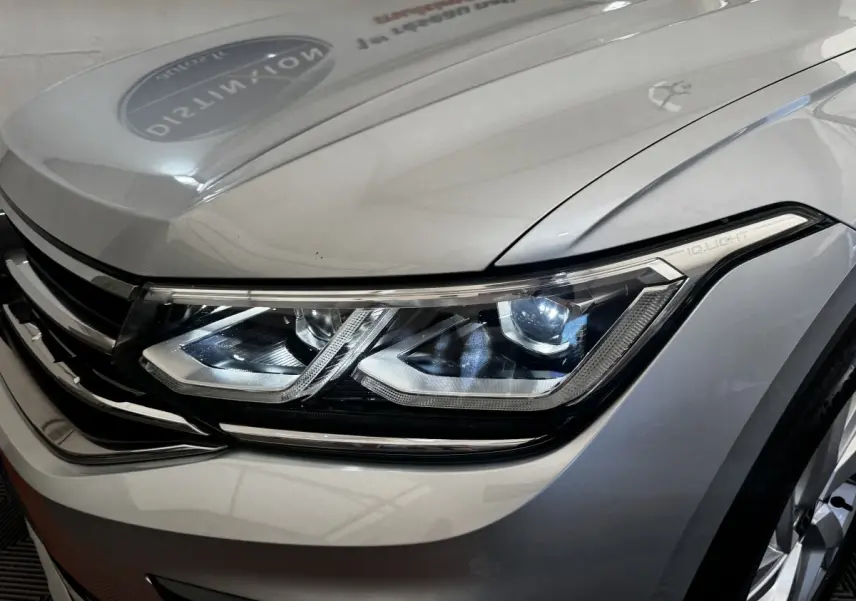 Gros plan sur le phare avant droit allumé du Volkswagen Tiguan gris clair, mettant en valeur la technologie IQ.Light.