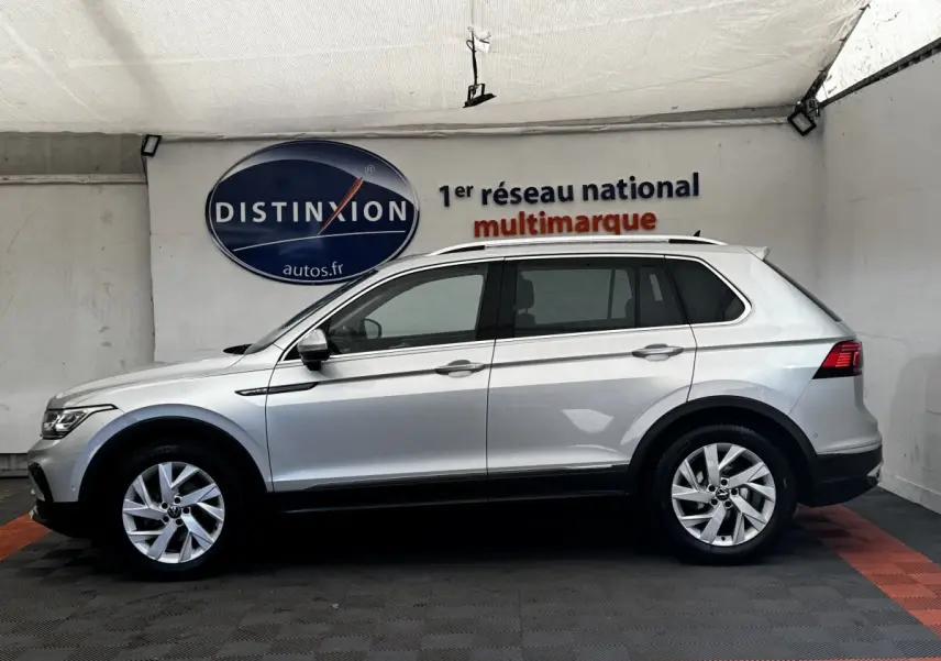 Vue latérale droite d'un Volkswagen Tiguan gris clair 2021, avec jantes alliage et barres de toit chromées visibles.