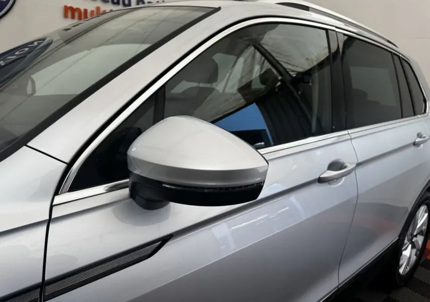 Vue rapprochée du côté gauche d’un Volkswagen Tiguan gris clair, mettant en valeur le rétroviseur et la porte avant.