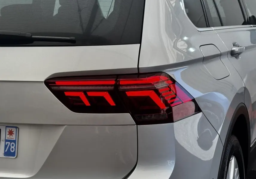Gros plan sur le feu arrière droit rouge d’un Volkswagen Tiguan gris clair, avec partie latérale et coffre visibles.