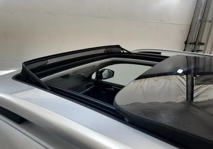 Vue rapprochée du toit ouvrant panoramique ouvert sur un Volkswagen Tiguan gris clair, intérieur partiellement visible.
