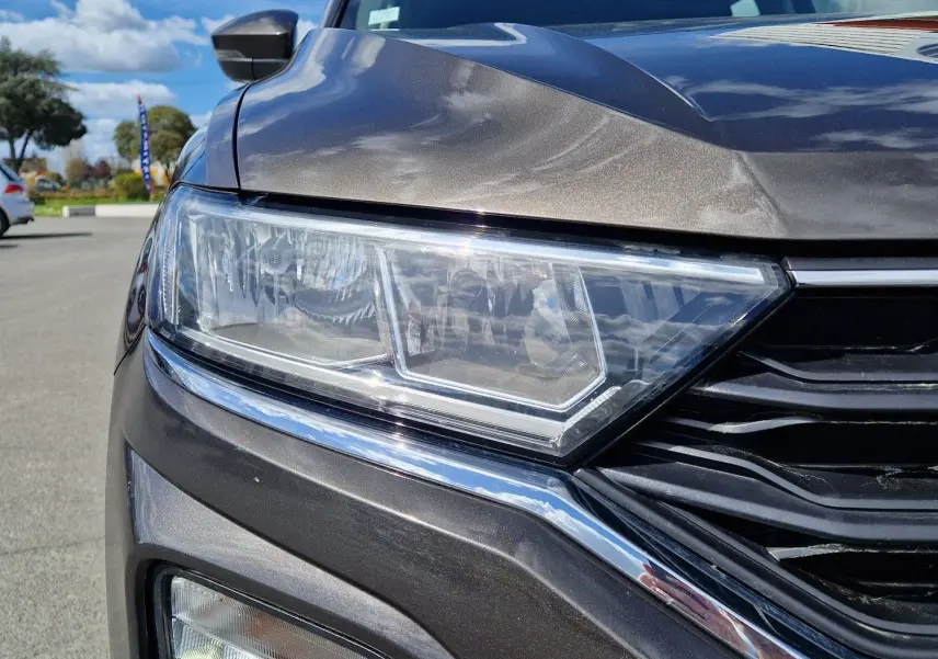 Gros plan sur le phare avant gauche du Volkswagen T-Roc Chêne Noir, soulignant ses feux LED et la calandre noire brillante.