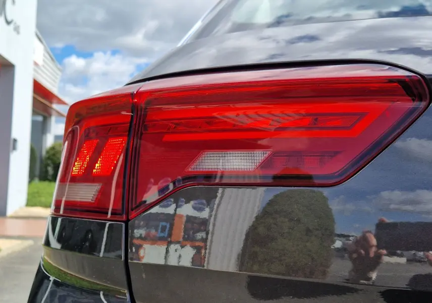 Gros plan sur le feu arrière gauche rouge du Volkswagen T-Roc Chêne Noir, reflétant l'environnement extérieur.