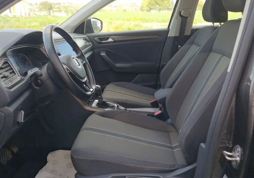 Vue intérieure côté conducteur du Volkswagen T-Roc Chêne Noir, mettant en valeur les sièges avant et le volant multifonction.