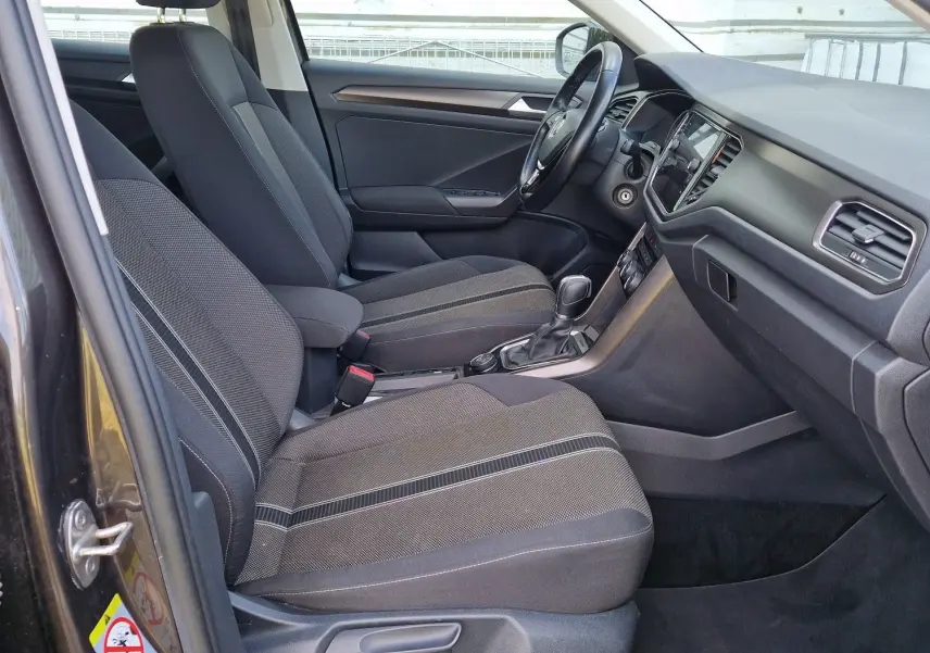 Vue intérieure côté conducteur du Volkswagen T-Roc chêne noir, montrant sièges avant et tableau de bord moderne.