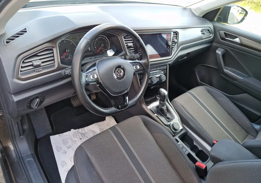 Vue intérieure côté conducteur du Volkswagen T-Roc noir, avec volant cuir multifonction et console centrale moderne.