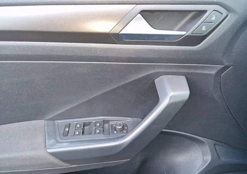Gros plan sur la porte côté gauche du Volkswagen T-Roc chêne noir, montrant les commandes électriques et la poignée intérieure.