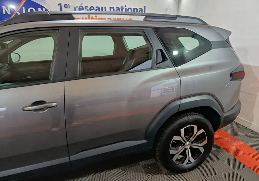 Vue latérale droite du Dacia Bigster gris foncé 2025 avec jantes alliage et barres de toit visibles.