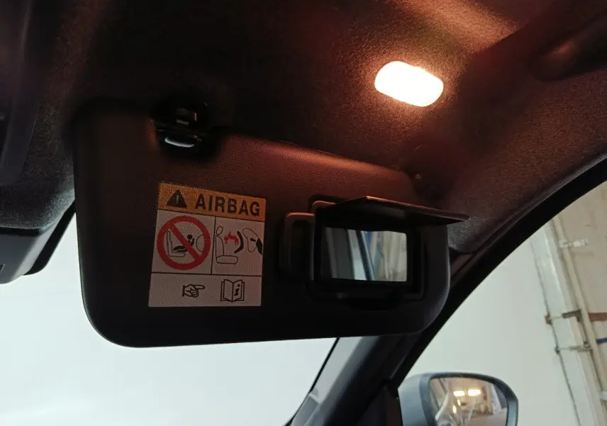 Détail intérieur du pare-soleil côté conducteur avec miroir et avertissement airbag, lumière allumée, rétroviseur visible.