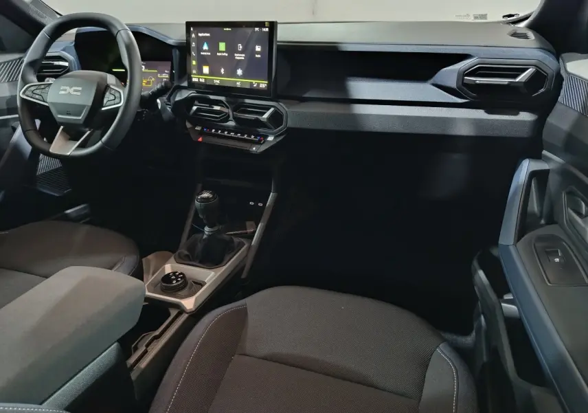 Vue intérieure côté conducteur du tableau de bord et console centrale du Dacia Bigster gris foncé avec écran tactile et boîte manuelle.