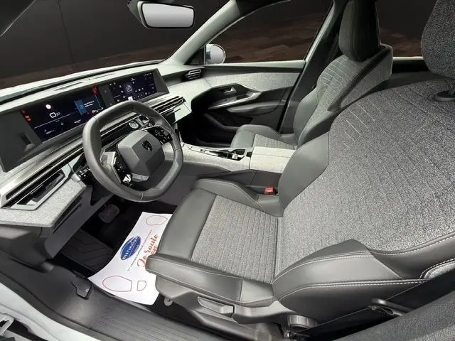Vue intérieure côté conducteur du Peugeot 5008 2025, sièges gris tissu et cuir, tableau de bord numérique large et moderne.