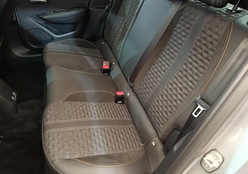 Vue intérieure de la banquette arrière en tissu et cuir noir avec surpiqûres orange d'une Peugeot 208 Electrique gris clair.