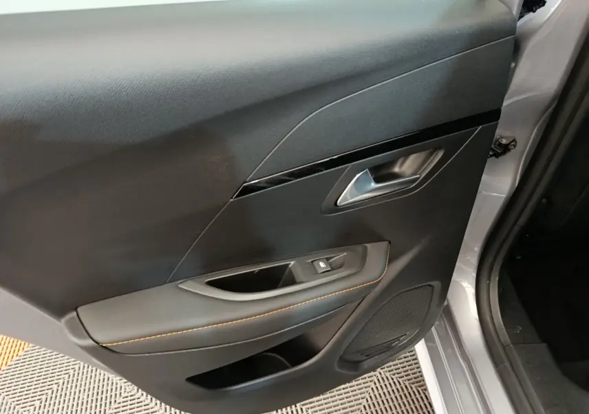 Vue rapprochée de la porte arrière droite gris clair du Peugeot 208 Electrique ROADTRIP avec poignée argentée et surpiqûres orange.